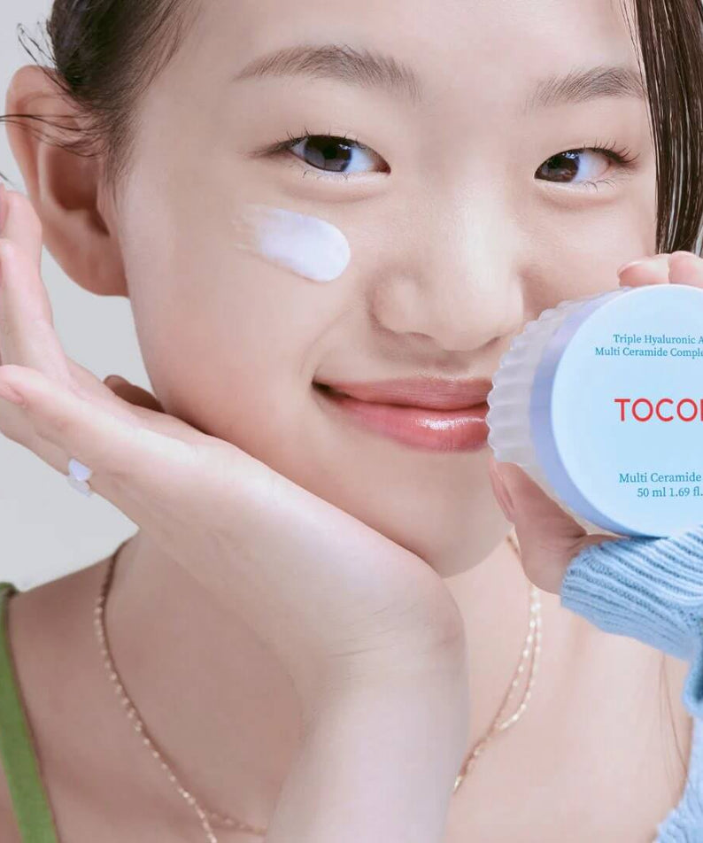 Smiling person applying TOCOBO Multi Caramide Cream to their face, holding a jar of the cream, showcasing skincare routine.