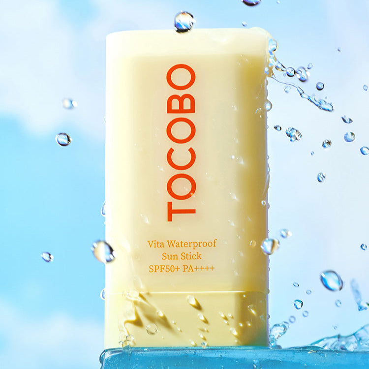 TOCOBO Vita Waterproof Sun Stick SPF50+ PA++++ with water droplets against a blue sky background.