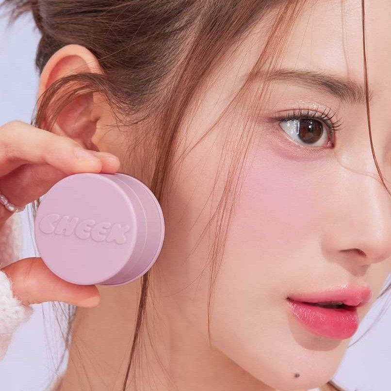Woman holding TONY MOLY Cheektone Jelly Blusher next to her face showcasing the product's texture and color.
