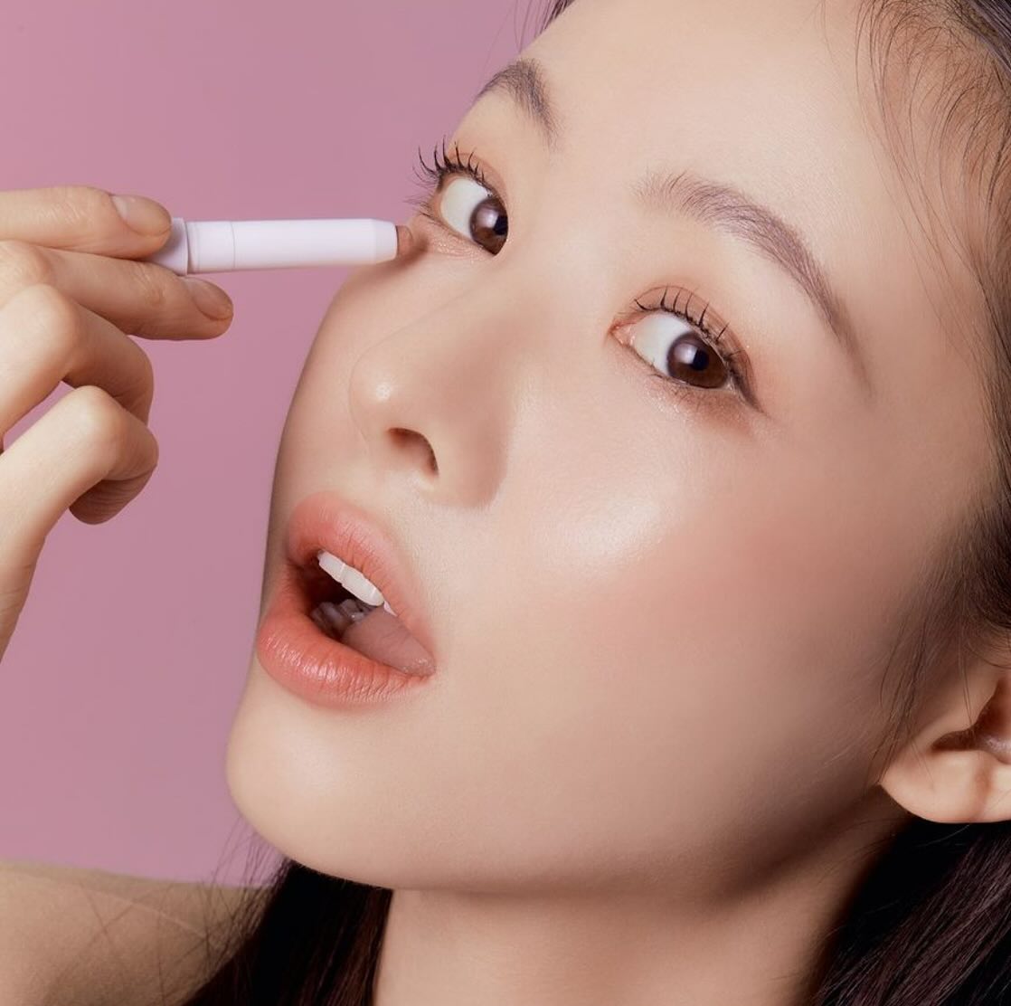 Woman applying TONY MOLY The Shocking Color Fixing Stick Shadow to eyelid with pink background.
