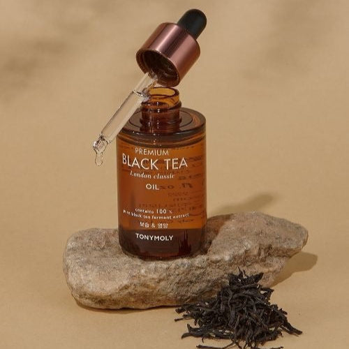 TONYMOLY Premium Black Tea London Classic Oil 35ml bottle with dropper on a rock with tea leaves.