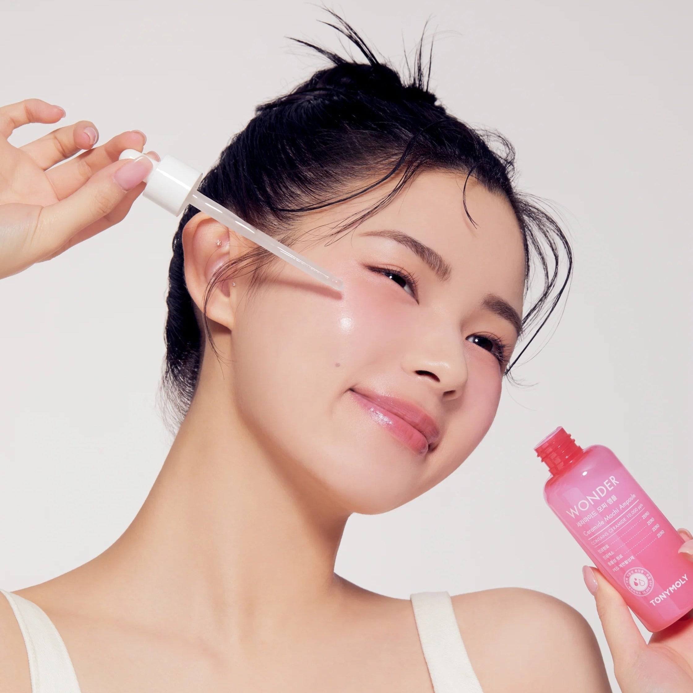 Woman applying TONYMOLY Wonder Ceramide Mochi Ampoule 100ml to face for glowing skin care routine.