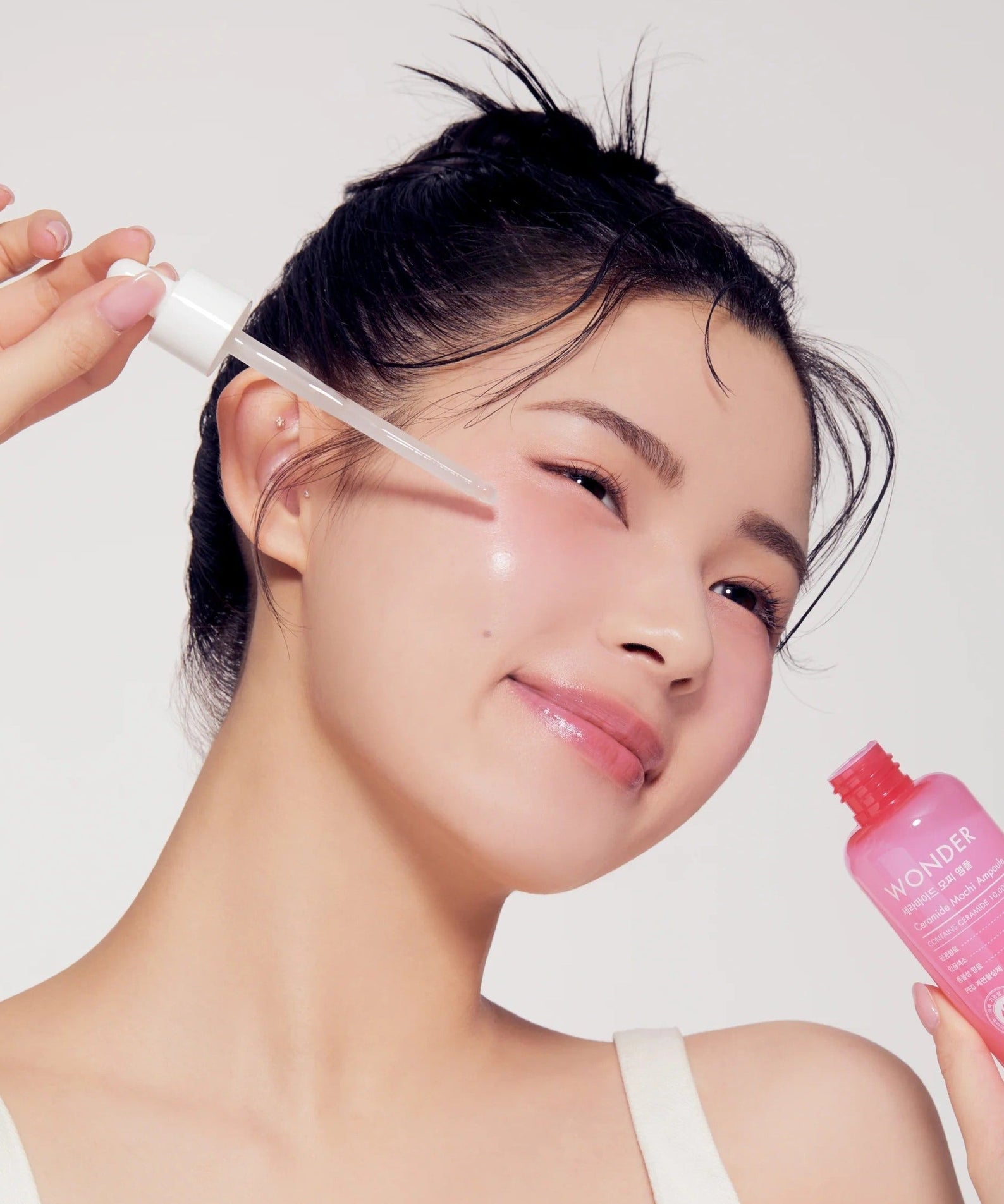 Woman applying TONYMOLY Wonder Ceramide Mochi Ampoule 100ml to face for glowing skin care routine.