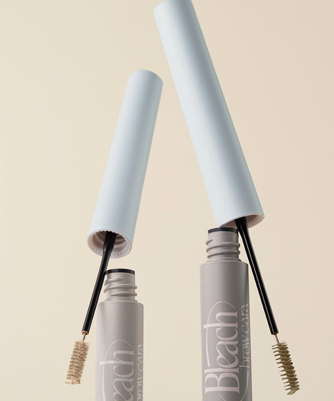 TOO COOL FOR SCHOOL Bleach Brow Cara, eyebrow mascara product image with open lids and brushes, beige background.