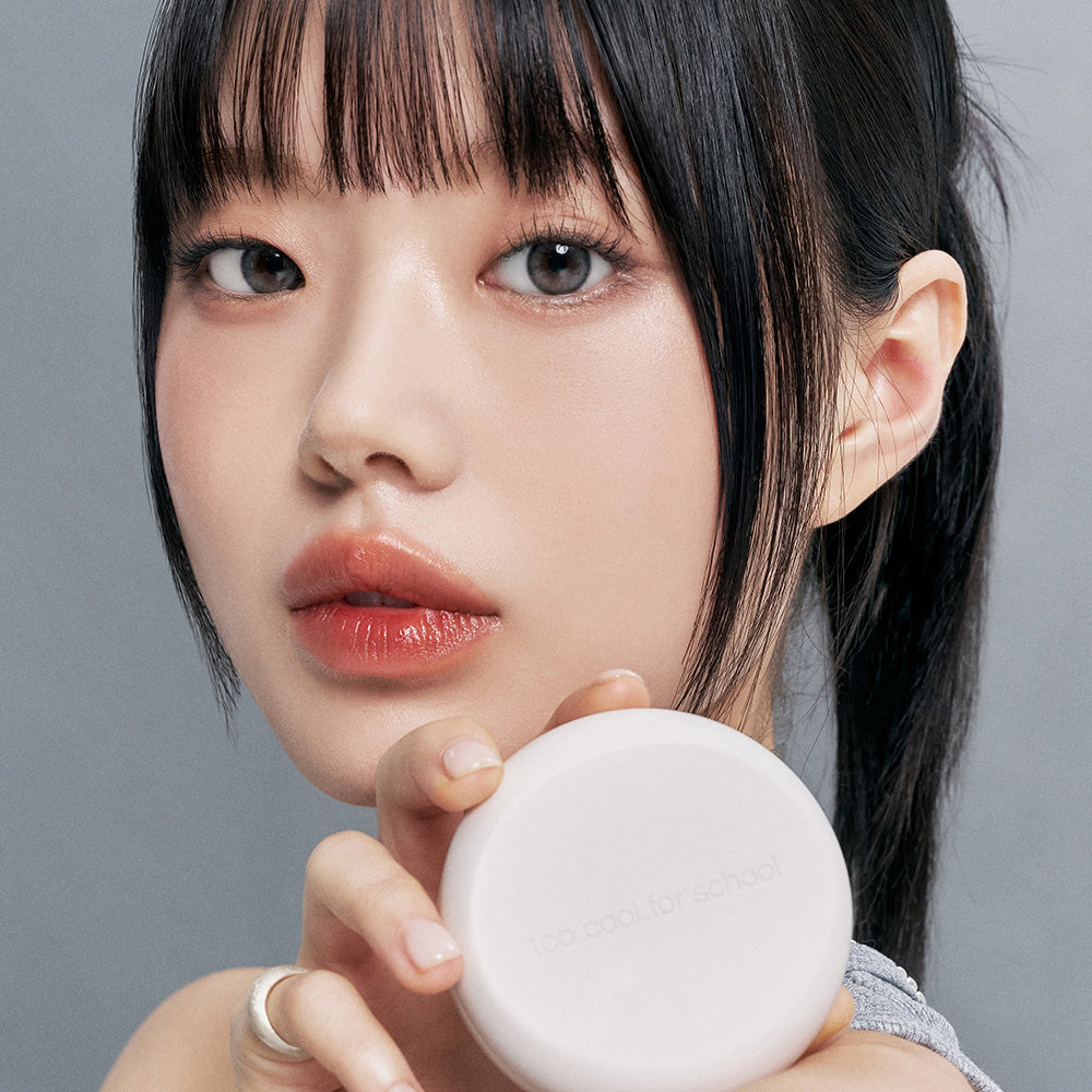 Model holding TOO COOL FOR SCHOOL Fixing Nude Fit Cushion [Product + Refill] showing product design and texture.