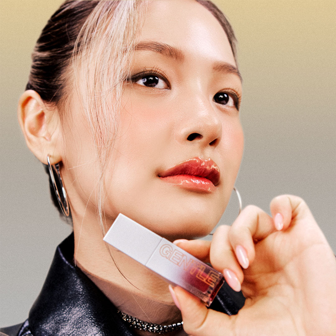 Model holding TOOQ Gentle Kiss Glow Tint with shimmering lip finish