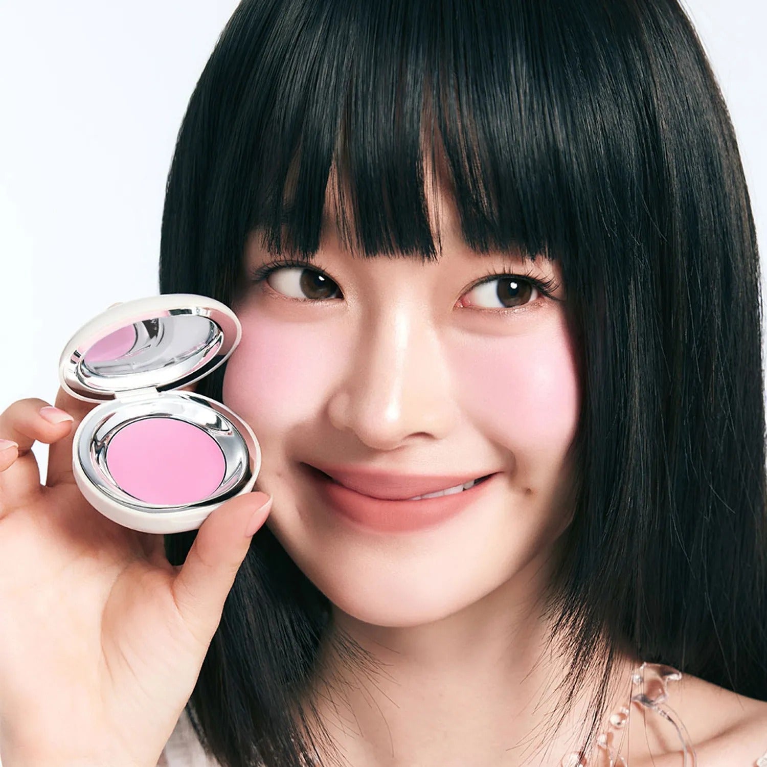Model applying TOOQ Satin Peach Blossom blush with a smile.