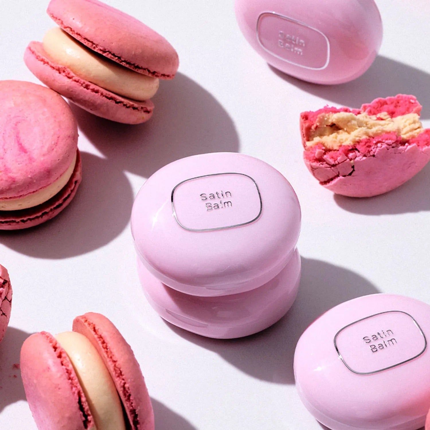 TOOQ Satin Peach Blossom balm surrounded by pink macarons, showcasing elegant packaging and pastel colors.
