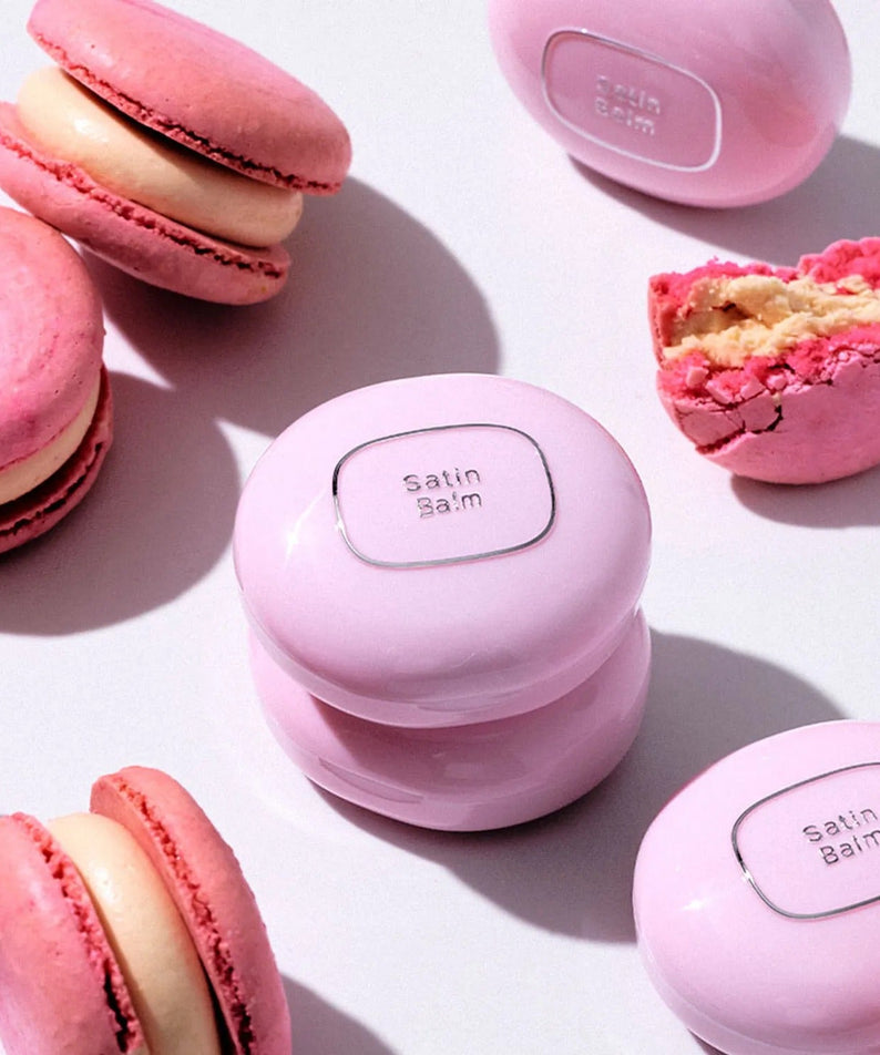 TOOQ Satin Peach Blossom balm surrounded by pink macarons, showcasing elegant packaging and pastel colors.