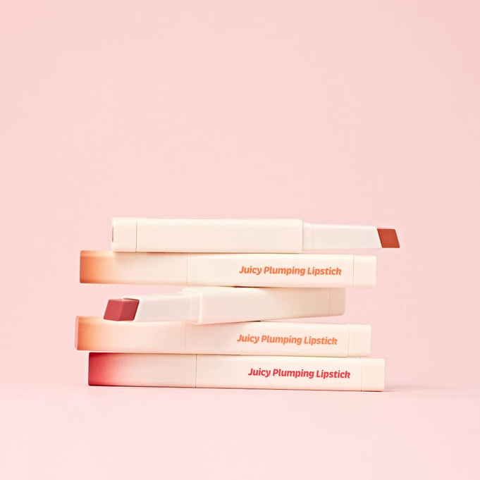 TOUCH IN SOL Vegan Again Juicy Plumping Lipstick displayed in a stack on a pink background.