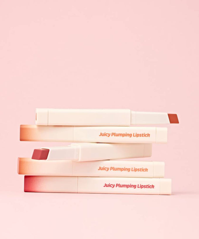 TOUCH IN SOL Vegan Again Juicy Plumping Lipstick displayed in a stack on a pink background.