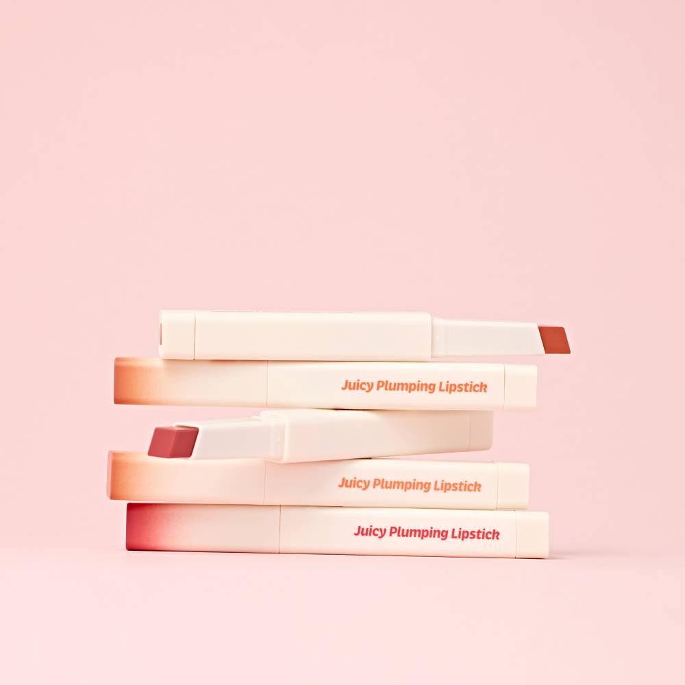 TOUCH IN SOL Vegan Again Juicy Plumping Lipstick displayed in a stack on a pink background.