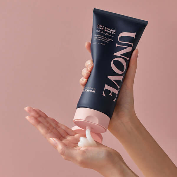 Hands holding UNOVE Deep Damage Treatment EX bottle against pink background.