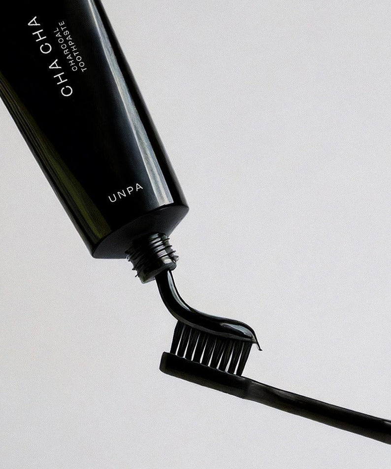 UNPA Cha Cha Charcoal Original Toothpaste 100g being squeezed onto a black toothbrush