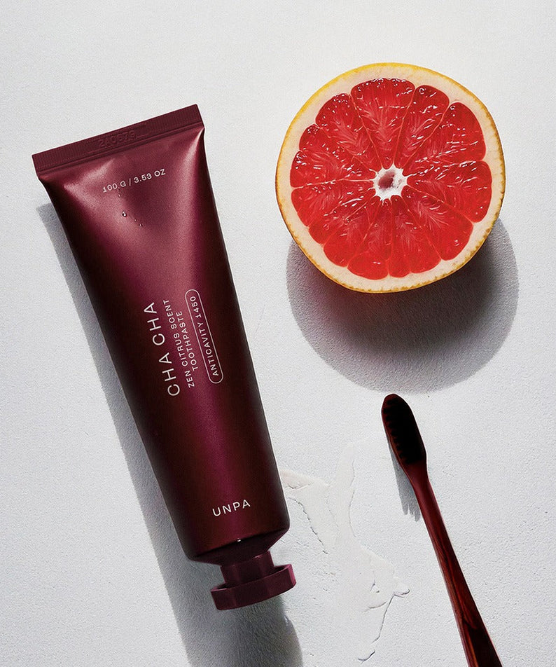 UNPA Cha Cha Zen Grapfruit Scent 1450 High Fluoride Toothpaste 100g with fresh grapefruit half and sleek toothbrush on surface.