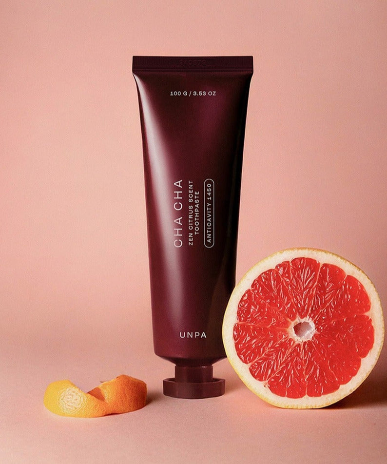 UNPA Cha Cha Zen Grapfruit Scent 1450 High Fluoride Toothpaste 100g tube with sliced grapefruit on a pink background