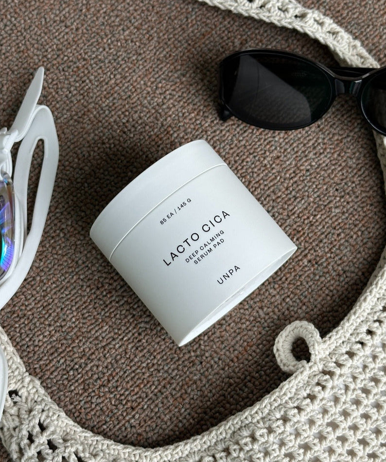 UNPA Lacto Cica Deep Calming Serum Pad 85 Sheets on a textured surface with sunglasses and a crochet bag.