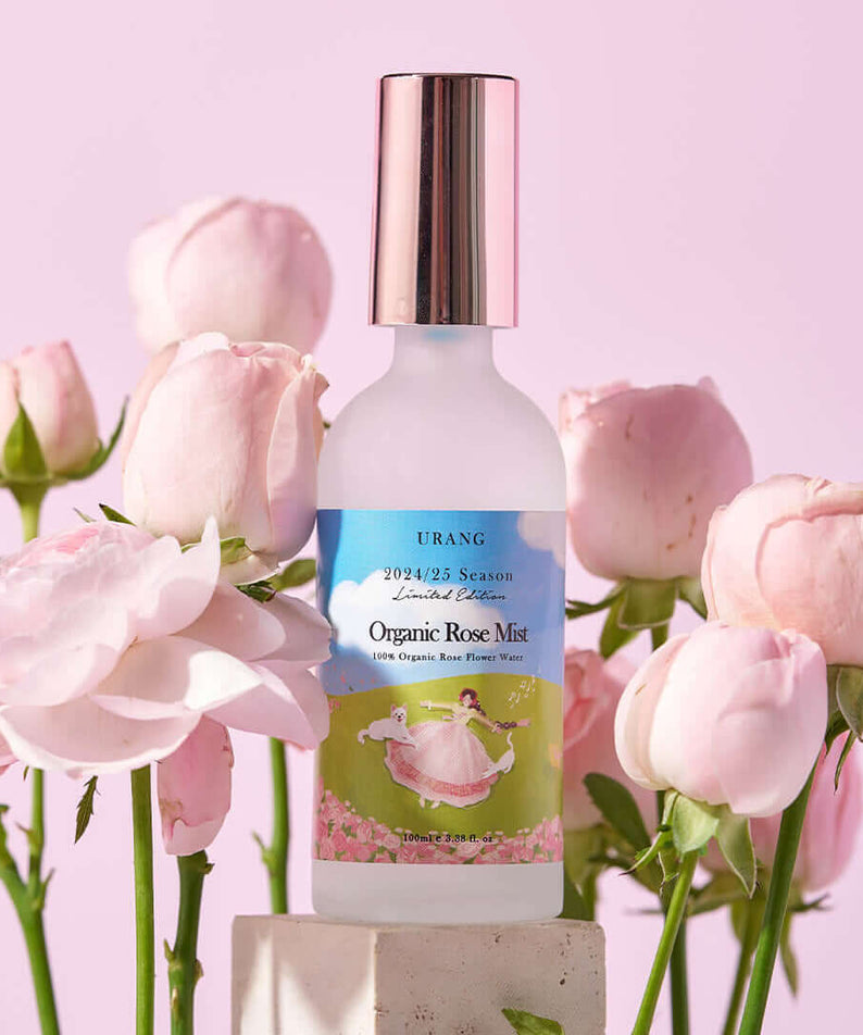 URANG Organic Rose Mist (2024/2025 Limited Edition) bottle surrounded by pink roses, displayed against a pink background.