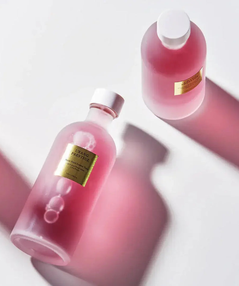 URANG Prestige Purple Shield Essence Toner bottles on a white surface with pink lighting.