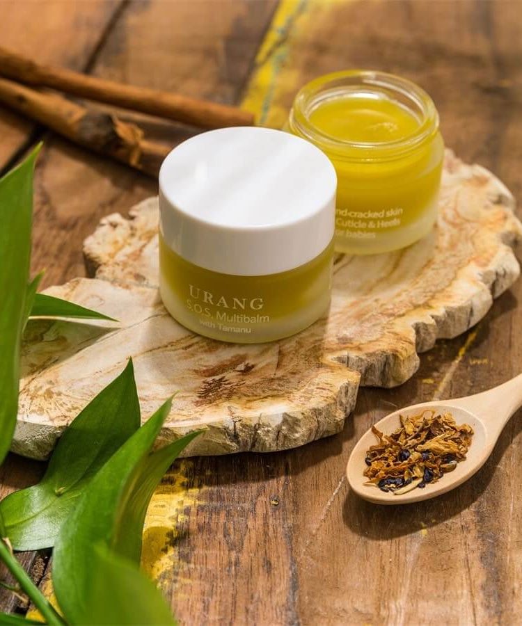 URANG SOS Multi Balm in a jar on a wooden surface with natural ingredients and foliage showcasing skincare benefits.