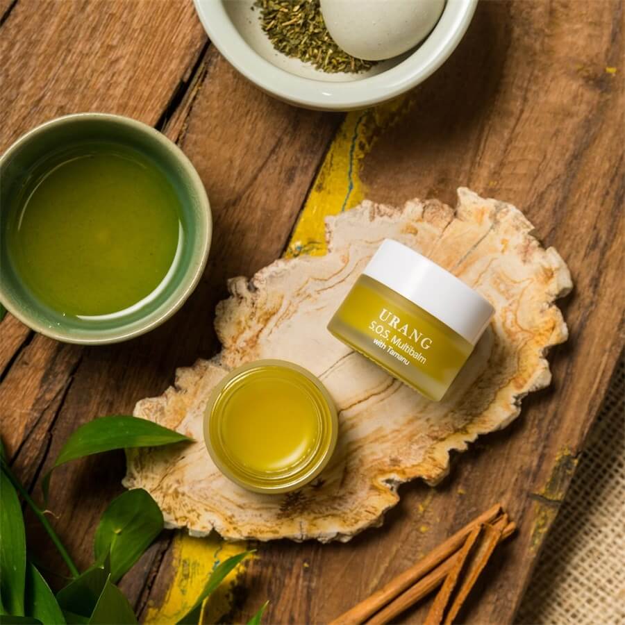 Image of URANG SOS Multi Balm jar with natural ingredients on a rustic wooden surface, showcasing the skincare product's natural appeal.