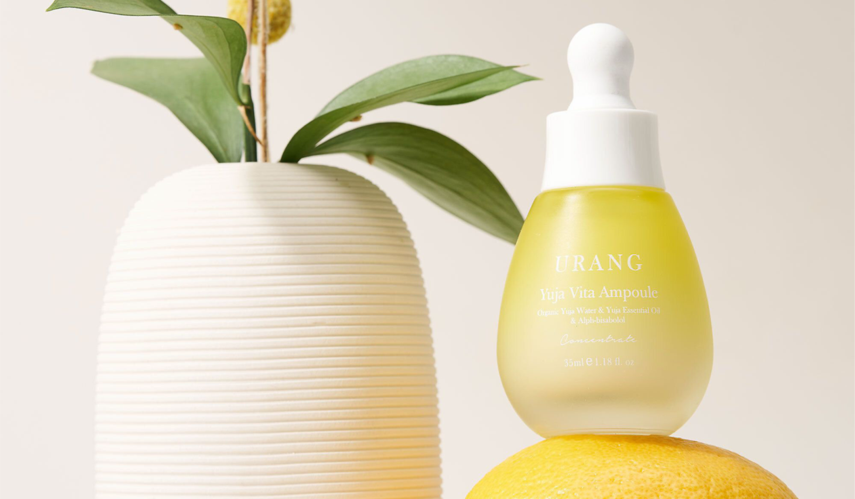 Urang Yuzu Vita Ampoule bottle with a green plant and lemon on a neutral backdrop, highlighting skincare and natural ingredients.