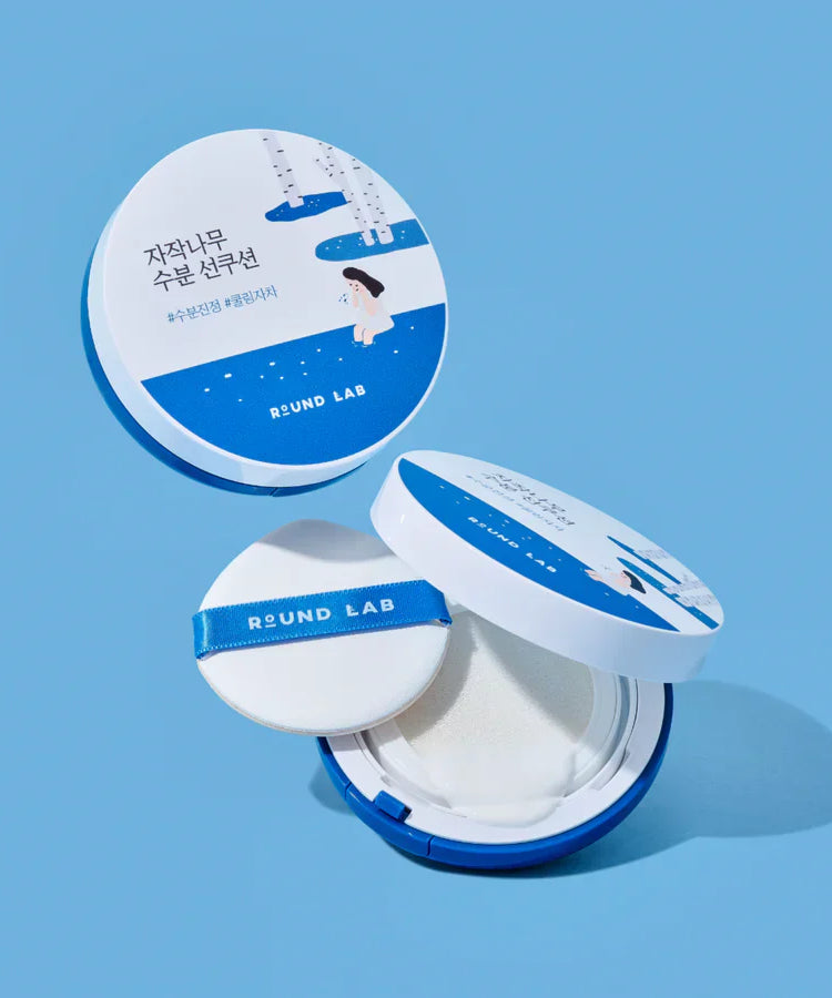 ROUND LAB Birch Juice Sun Cushion 15g with open compact and puff against blue background.