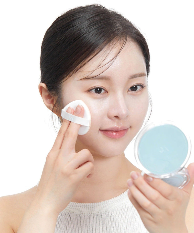 Woman applying VT COSMETIC PDRN Essennce Glow Sun Pact 10g with puff, using compact mirror for even application.