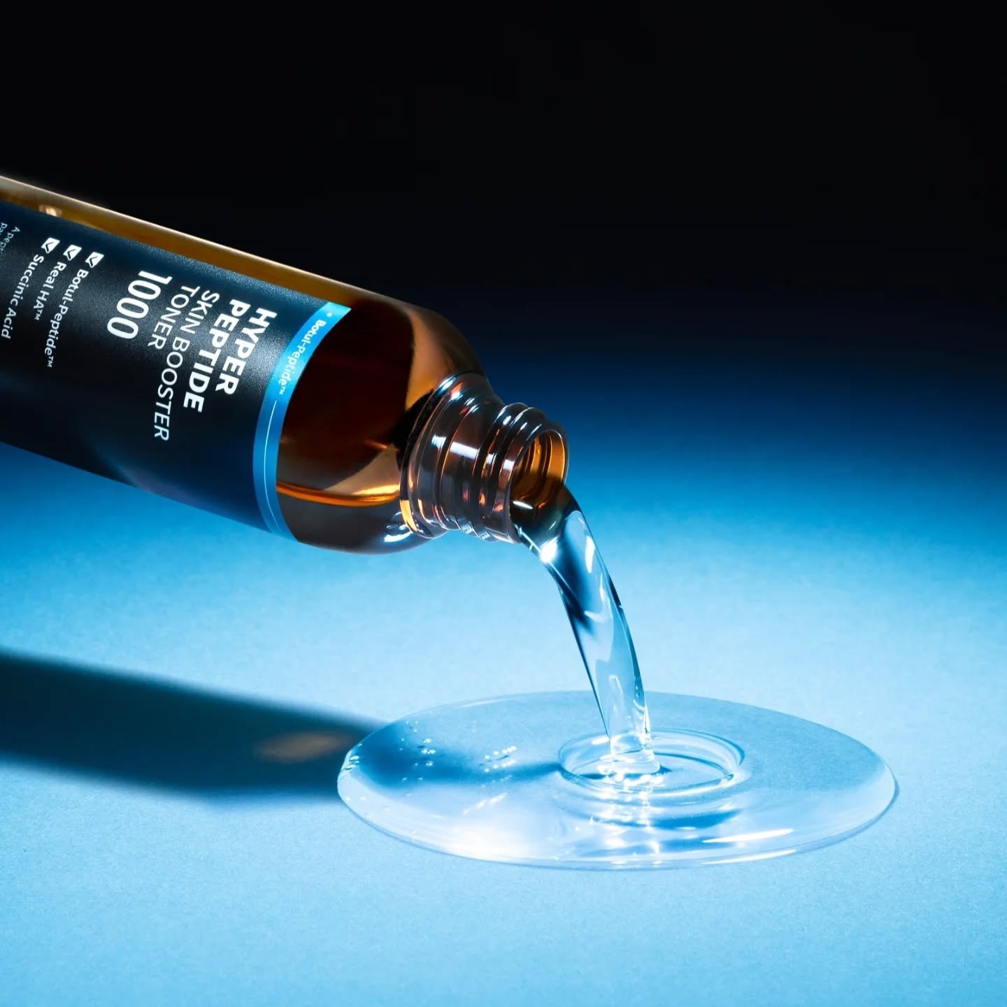 WELLAGE Hyper eptide Skin booster Toner 200ml being poured onto a blue surface, showcasing the liquid texture and premium packaging.
