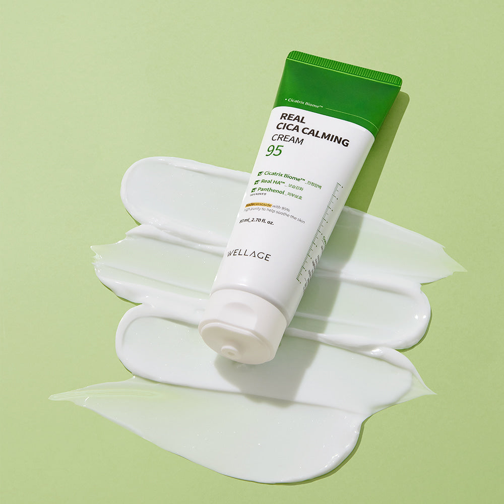 WELLAGE Real Cica Calming 95 Cream 80ml tube on a green background with a smear of cream