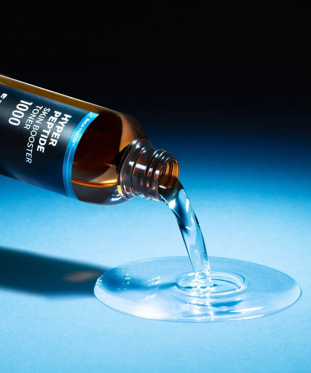WELLAGE Hyper eptide Skin booster Toner 200ml being poured onto a blue surface, showcasing the liquid texture and premium packaging.