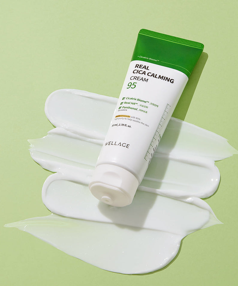 WELLAGE Real Cica Calming 95 Cream 80ml tube on a green background with a smear of cream