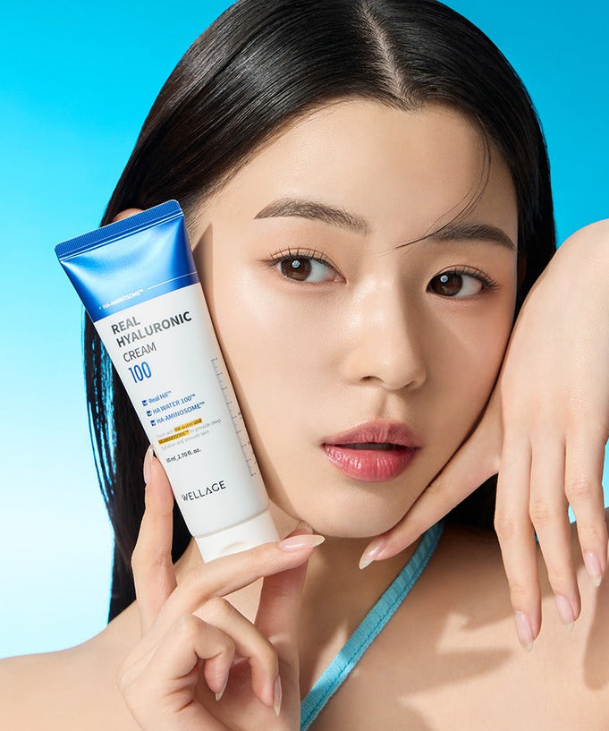 WELLAGE Real Hyaluronic 100 Cream 80ml held by model against blue background, showcasing skincare product.
