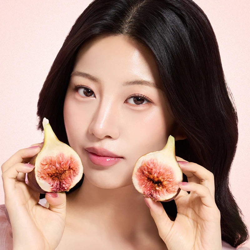 Woman holding sliced figs against face on pastel background