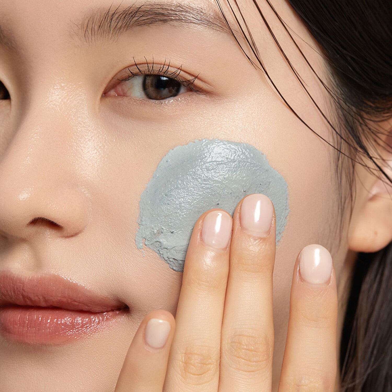 Woman applying WHIPPED Mugtree Vegan Cookie Clay Pack Cleanser 180ml on her cheek for skincare routine.