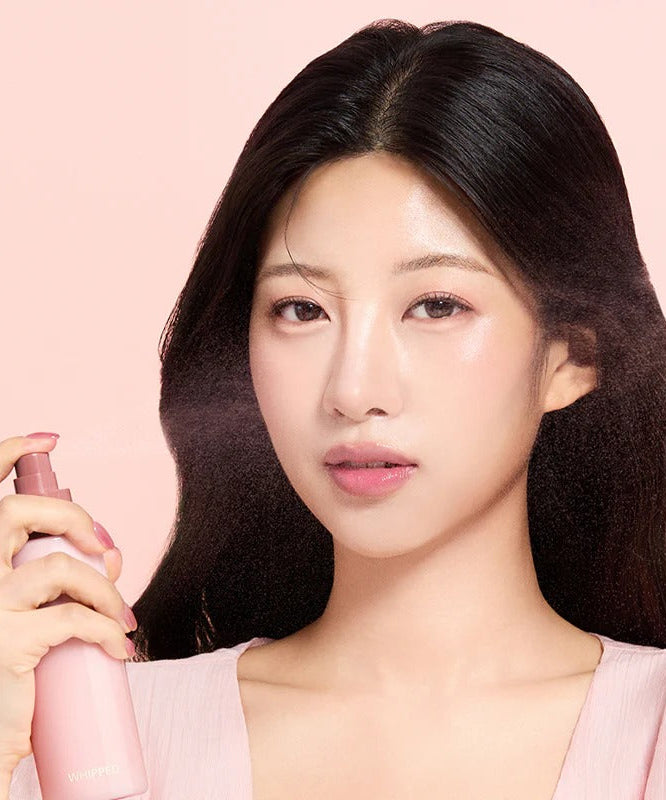 Model holding WHIPPED Butter Vegan Milk Foam Pack Mist 150ml product bottle against pink background.