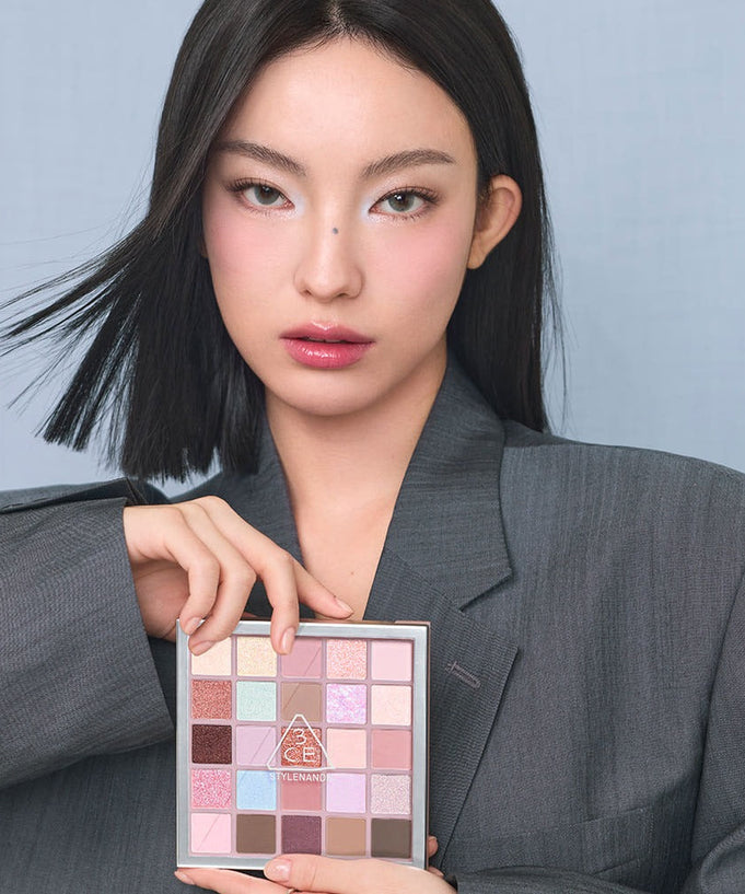 Model holding 3CE XL Eyeshadow Palette with diverse color selection in sleek packaging, showcasing makeup possibilities.