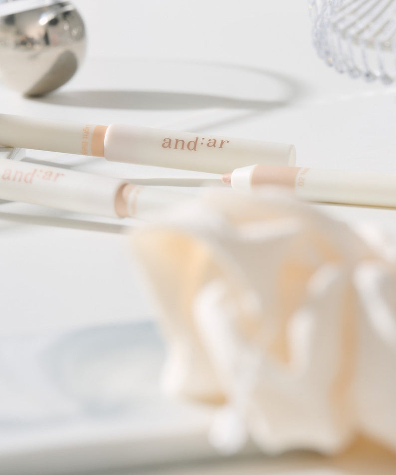 Close-up of the AND:AR Soft Skinfit Dual Concealer Pencil on a white surface, showcasing its sleek design and dual-end functionality.