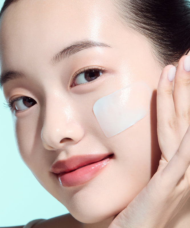 Woman applying skincare product to face on a light blue background.