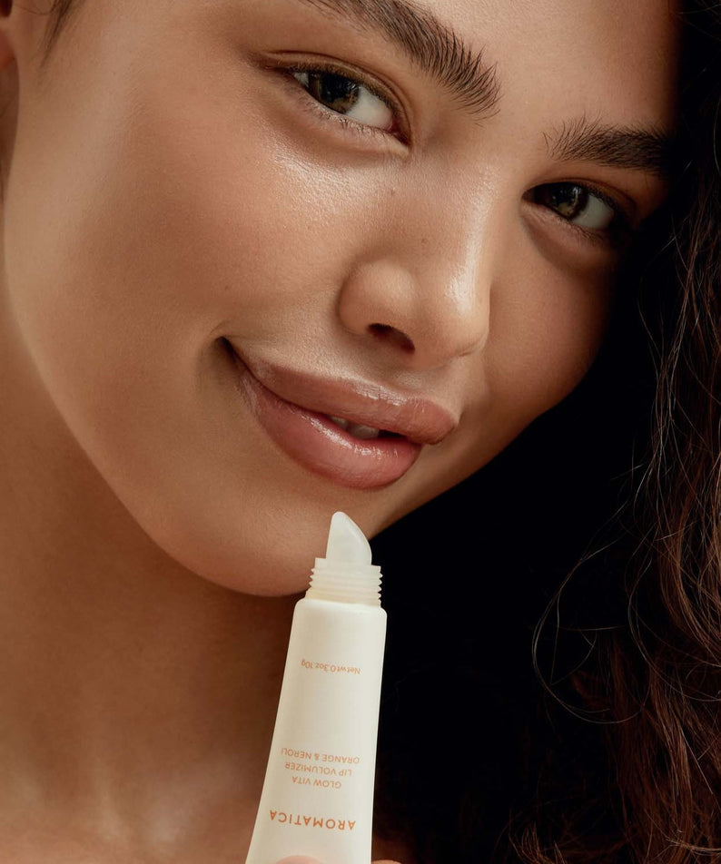 Woman applying AROMATICA Glow Vita Lip Volumizer Orange & Neroli for a plump, vibrant look.