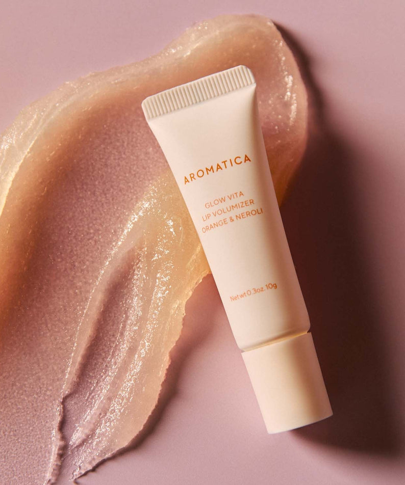 AROMATICA Glow Vita Lip Volumizer Orange & Neroli product on a textured background