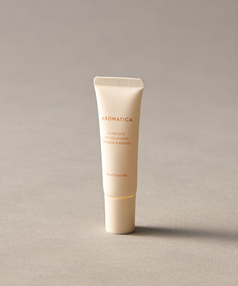AROMATICA Glow Vita Lip Volumizer Orange & Neroli tube on a neutral background