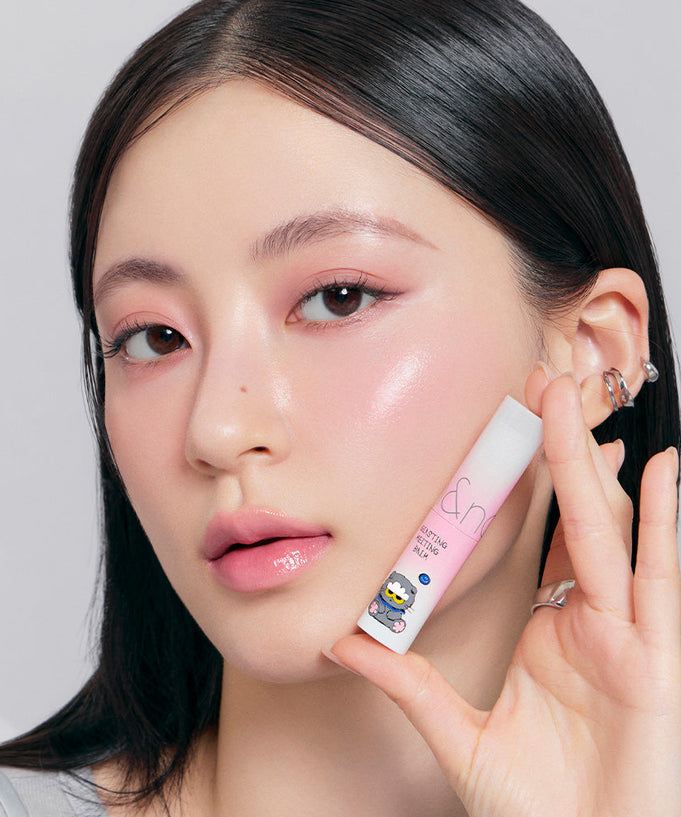 Woman holding ROMAND x Joanne Friends Glasting Melting Balm with pink packaging and cartoon character design.
