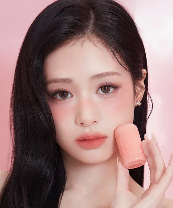 Woman holding BANILA CO Romantic Blush Lip & Cheek, showing makeup results on her face.