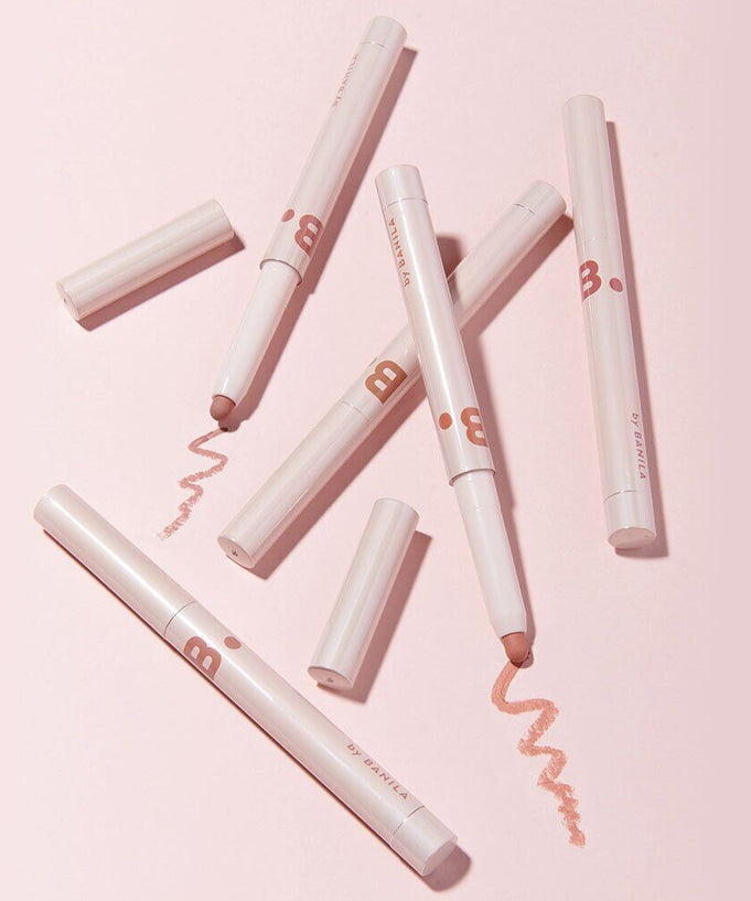Assorted BANILA CO Smudging Lip Pencil on pink background, showcasing their applicator tips and design.