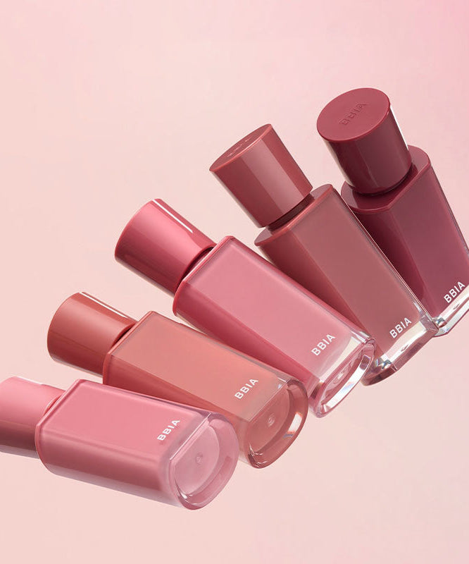 Assorted shades of BBIA Glow Tint bottles on a pink background
