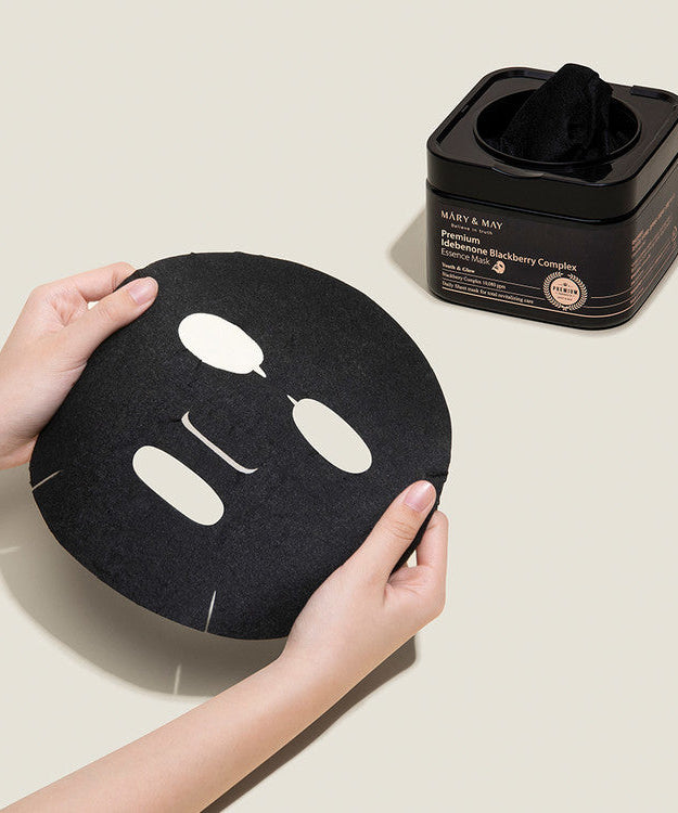 Hands holding MARY & MAY Premium Idebenone Blackberry Complex Essence Mask x20 with mask container in background.