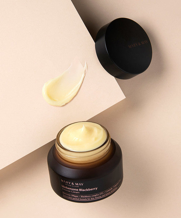 Open jar of MARY & MAY Idebenone Blackberry Intense Cream 70g with cream swatch on beige background.