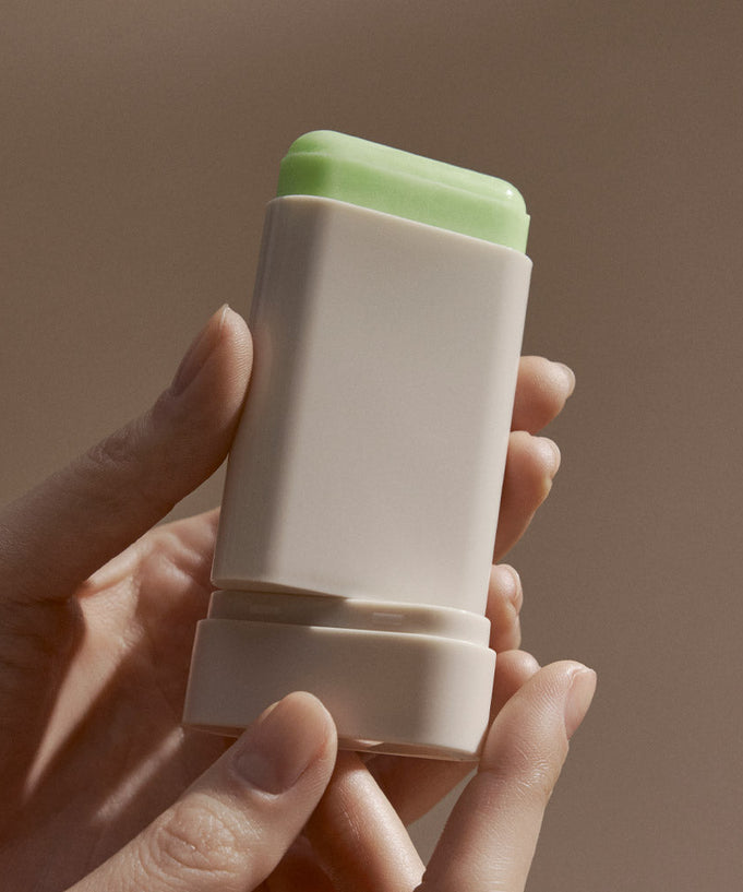 BLITHE Ice Sunscreen Stick held in hand, showing the product's design and green top in a neutral background setting.