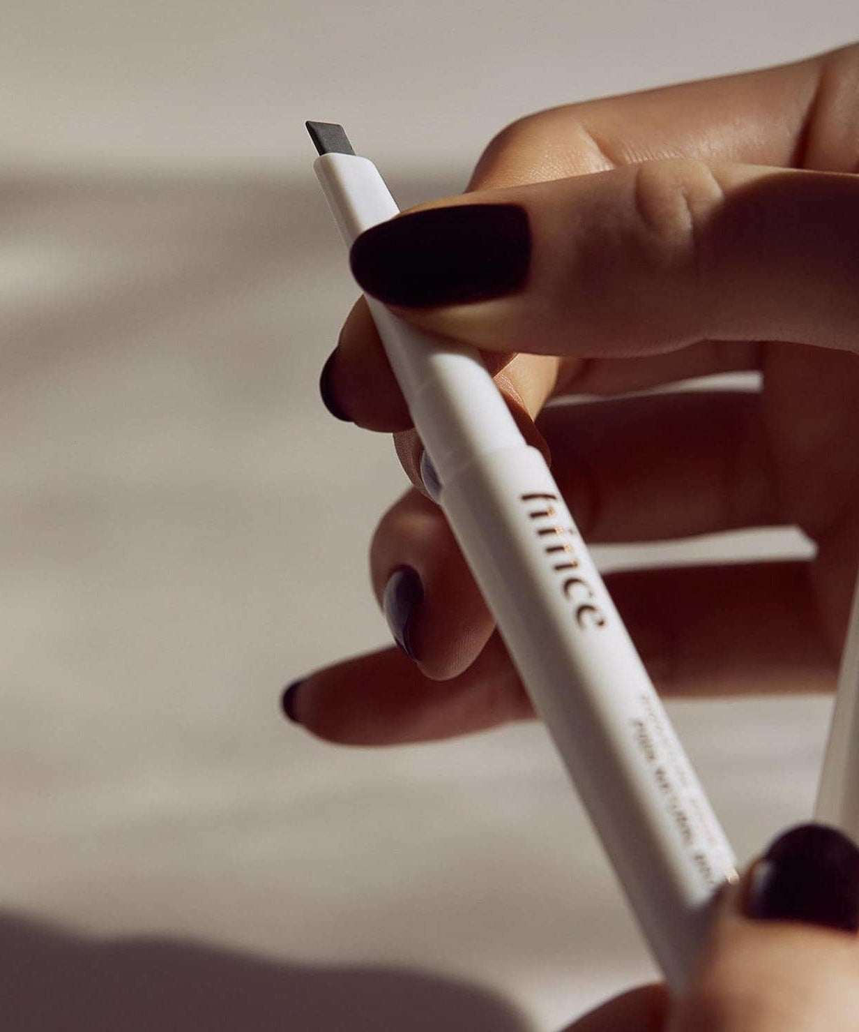 Person holding HINCE Signature Brow Pencil with black nails.